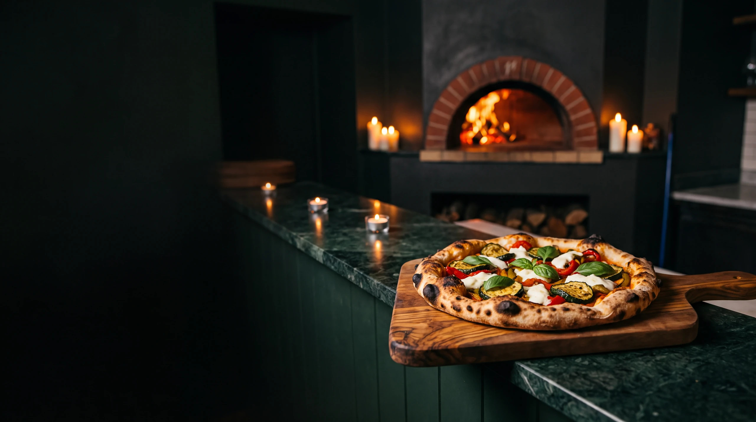 A wood-fired flatbread on an olive-wood board in front of the glowing oven